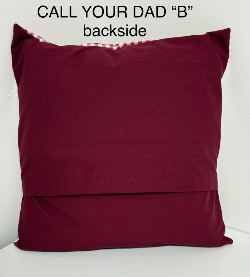 May include: Burgundy red pillow with a white and red checkered fabric on the back. The pillow has the text "CALL YOUR DAD "B"" printed on the front.