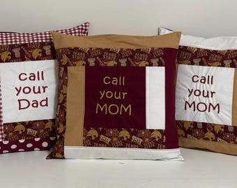 May include: Five decorative throw pillows with a patchwork design. The pillows are made of a variety of fabrics, including red, white, and brown. The pillows have embroidered text that reads "Call your Dad" and "Call your Mom".