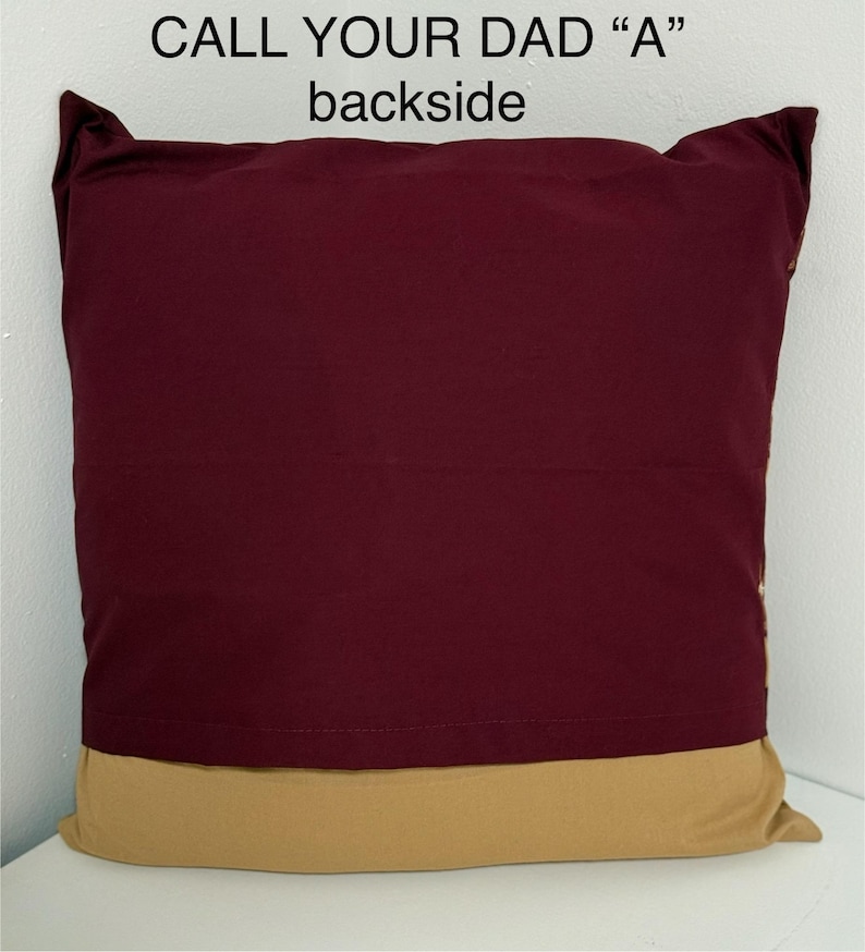 May include: A burgundy pillow with a gold trim. The back of the pillow has the text "CALL YOUR DAD "A"" printed on it.