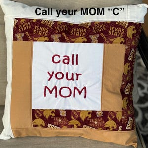 May include: A white pillow with a brown and maroon patchwork design. The pillow has the words "Call your MOM "C"" embroidered on the top and "call your MOM" embroidered in red on the front.