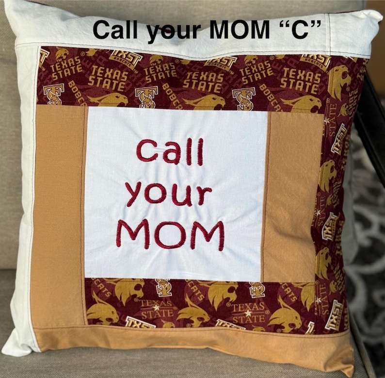 May include: A white pillow with a brown and maroon patchwork design. The pillow has the words "Call your MOM "C"" embroidered on the top and "call your MOM" embroidered in red on the front.