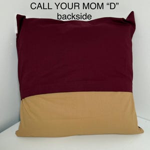 May include: A burgundy and tan pillow with the text "CALL YOUR MOM "D"" printed on the front. The back of the pillow is tan.