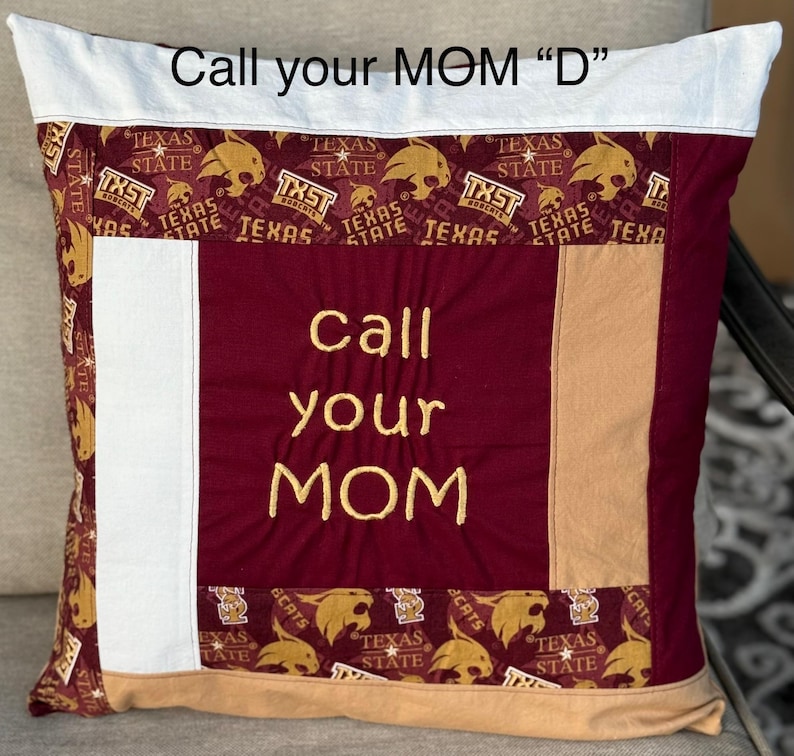 May include: A maroon and tan pillow with a white border. The pillow is decorated with a patchwork of fabric featuring the Texas State University logo and the words "Call your MOM" embroidered in gold thread.