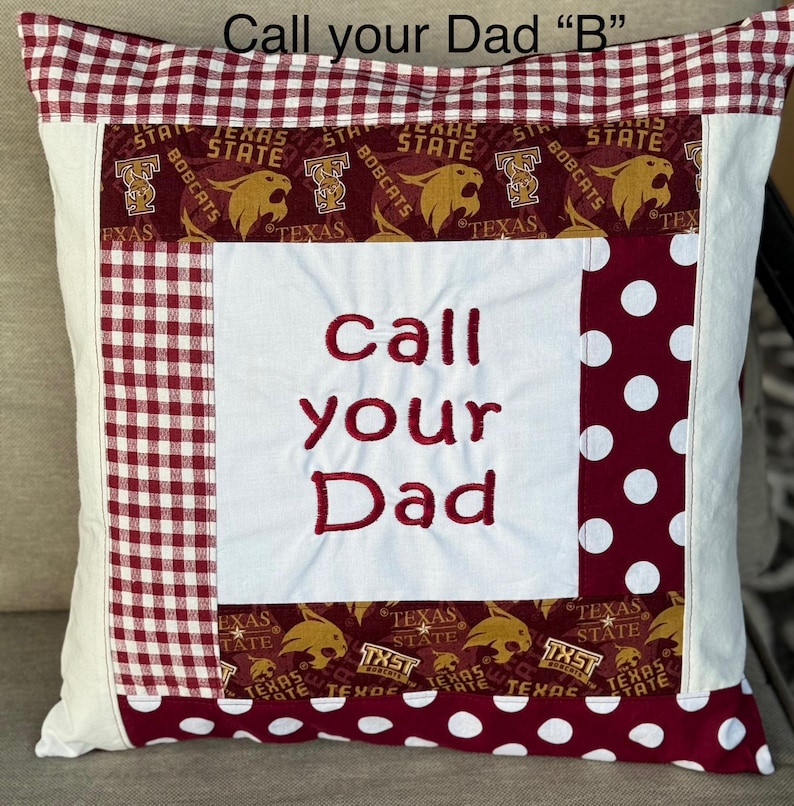 May include: A white pillow with a red and white checkered border and a red and white polka dot border. The center of the pillow has a white fabric with the words "call your Dad" embroidered in red. The pillow is decorated with a red and gold fabric with the words "Texas State Bobcats" repeated.