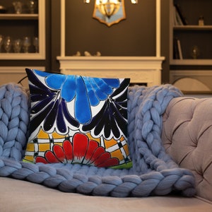 May include: A colorful throw pillow with a geometric pattern featuring black, blue, red, yellow, and white colors. The pillow is on a blue knitted throw blanket.