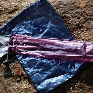 May include: Two silver spoons are wrapped in a purple and blue waterproof pouch. The pouch is made of a lightweight, durable material and is ideal for storing and protecting utensils.