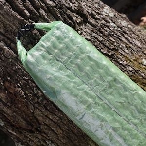 Op de afbeelding: Een groene waterdichte droge tas met een zwarte clip sluiting. De tas is gevouwen en opgerold, en de clip is gesloten.