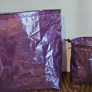 Peut inclure: Deux sacs à cordon de couleur violette en tissu léger et iridescent. Le plus grand sac est plus grand et plus large que le plus petit.