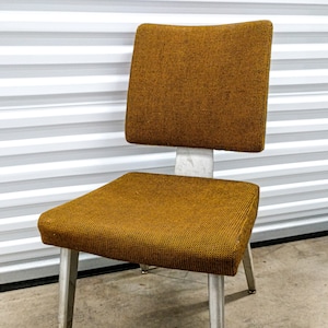 May include: A brown upholstered chair with a metal frame and legs. The chair has a slightly curved back and a comfortable seat.