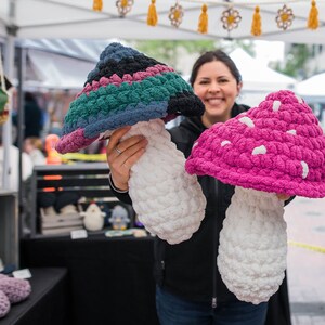 May include: Two crocheted mushroom-shaped plushies. One is a multi-colored mushroom with a white stem. The other is a pink mushroom with white spots and a white stem.