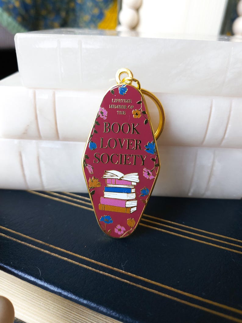 May include: A red metal keychain shaped like a motel sign with the text "Lifetime Member of the Book Lover Society" and a stack of books with floral accents.