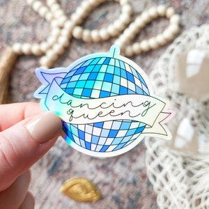 May include: A holographic sticker featuring a blue and white disco ball with the text "dancing queen" on a white banner.