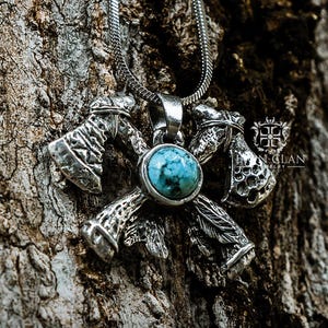 May include: Silver Axe Totem pendant necklace with a turquoise centre stone. The pendant features four axes arranged in a cross shape, with detailed carvings. The necklace is set against a textured tree bark background.