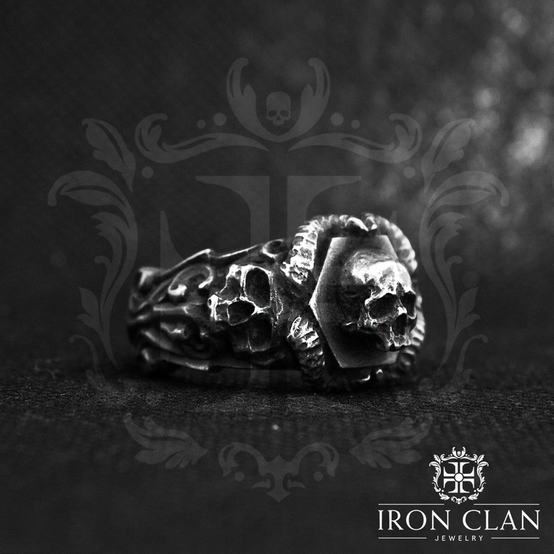 May include: A silver ring with a skull design. The ring is detailed with intricate carvings and a hexagonal center piece. The ring is made by Iron Clan Jewelry.
