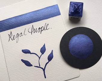 May include: A close-up of a swatch of Regal Purple ink on white paper, a small ink cube, and a black circle with a purple ink dot. The words "Regal Purple" are handwritten on the paper, along with a small illustration of a plant.