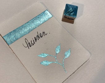 May include: A teal watercolor paint cube with the word "Poseidon" on the side. A sample card with a teal glitter stripe and a teal leaf design. The word "Poseidon" is handwritten on the card.