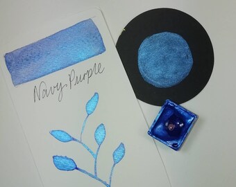 May include: A sample of Navy Purple ink in a small pan. The ink is a deep blue with a shimmery finish. The ink is shown on a white card with the words "Navy Purple" written in black ink.