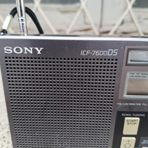 May include: A dark gray Sony ICF-7600DS radio with a retractable antenna. The radio has a speaker grill, a digital display, and control buttons for tuning and scanning. The text "SONY" and "ICF-7600DS" are visible on the front.