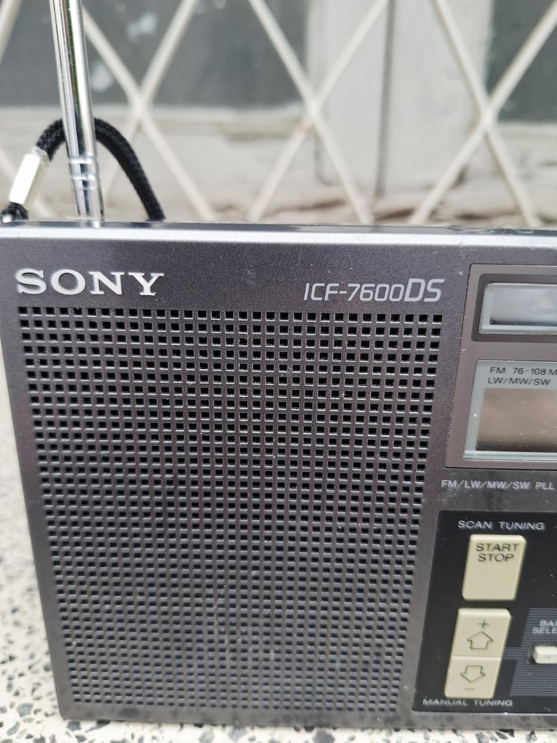 May include: A dark gray Sony ICF-7600DS radio with a retractable antenna. The radio has a speaker grill, a digital display, and control buttons for tuning and scanning. The text "SONY" and "ICF-7600DS" are visible on the front.