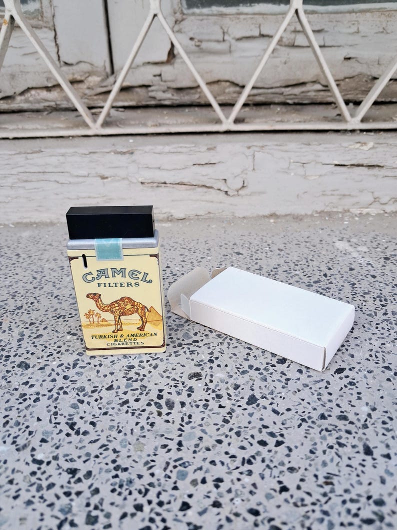 Puede incluir: Un paquete de cigarrillos vintage Camel Filters con una ilustraci&oacute;n de camello y el texto "Turkish & American Blend Cigarettes". El paquete est&aacute; cerrado y se encuentra sobre una superficie blanca.