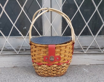 May include: A woven wicker basket with a blue fabric lining and red leather accents. The basket has two handles and a hinged lid.