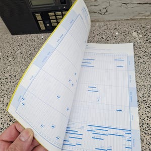 May include: A black ICF-7600DS radio sits next to an open book with blue and white charts and graphs. The book's pages are yellowed, and the text includes "Europe", "Middle East", "Asia Oceania", "Africa", and "America".