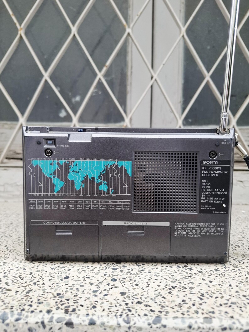 May include: A gray Sony ICF-7600DS radio receiver with a retractable antenna. The front panel features a world map graphic in teal, a frequency scale, and text including "TIME SET" and "RADIO BATTERY".