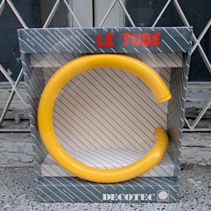 Puede incluir: Una letra C de plástico amarilla en una caja con el texto "LE TUBE" y "DECOTEC" en ella.