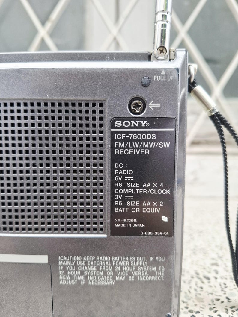 May include: A silver Sony ICF-7600DS FM/LW/MW/SW receiver radio. The radio has a pull-up antenna and a black label with text including "MADE IN JAPAN". The radio requires 4 AA batteries or equivalent.