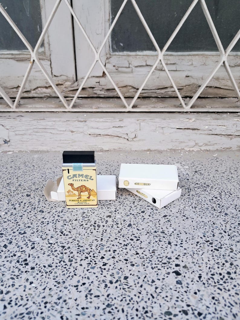May include: A pack of Camel Filter cigarettes with a camel illustration and the text "TURKISH & AMERICAN BLEND" on the front. The pack is sitting on a white surface.