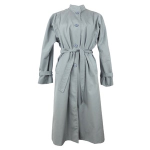 May include: A long, light gray trench coat with a button-up front and a matching belt. The coat has a stand-up collar and long sleeves.