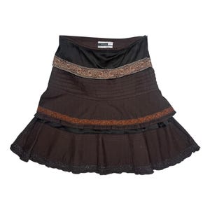 May include: A brown and black tiered skirt. The skirt has a black waistband and decorative trim with a patterned design. The skirt has a flared silhouette and is made of a lightweight fabric.