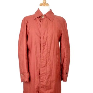 May include: A long, rust-colored quilted coat with a button closure and a collar. The coat is on a mannequin.