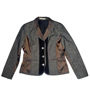Pode incluir: Um blazer sob medida com um design único. O casaco apresenta um padrão xadrez cinza nas mangas e nas costas, com painéis de cetim marrom nas laterais e um centro de veludo preto. Possui três botões brancos.