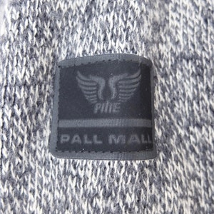 May include: A black and white knit sweater with a black patch on the front. The patch has a white logo with a winged design and the text "PALL MALL" underneath.