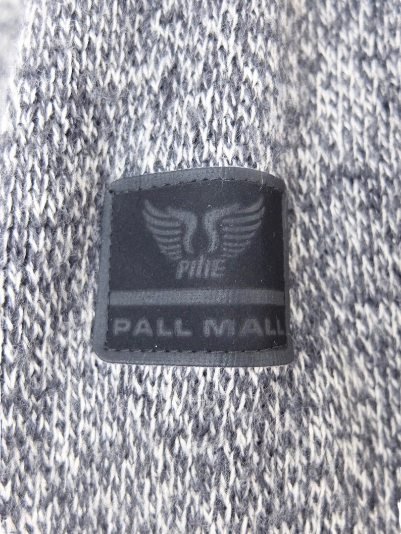 May include: A black and white knit sweater with a black patch on the front. The patch has a white logo with a winged design and the text "PALL MALL" underneath.