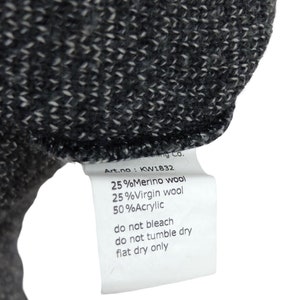 May include: A white tag with black text detailing the fabric composition and care instructions for a garment. The tag reads: "Art.no: KW1832 25%Merino wool 25%Virgin wool 50%Acrylic do not bleach do not tumble dry flat dry only"