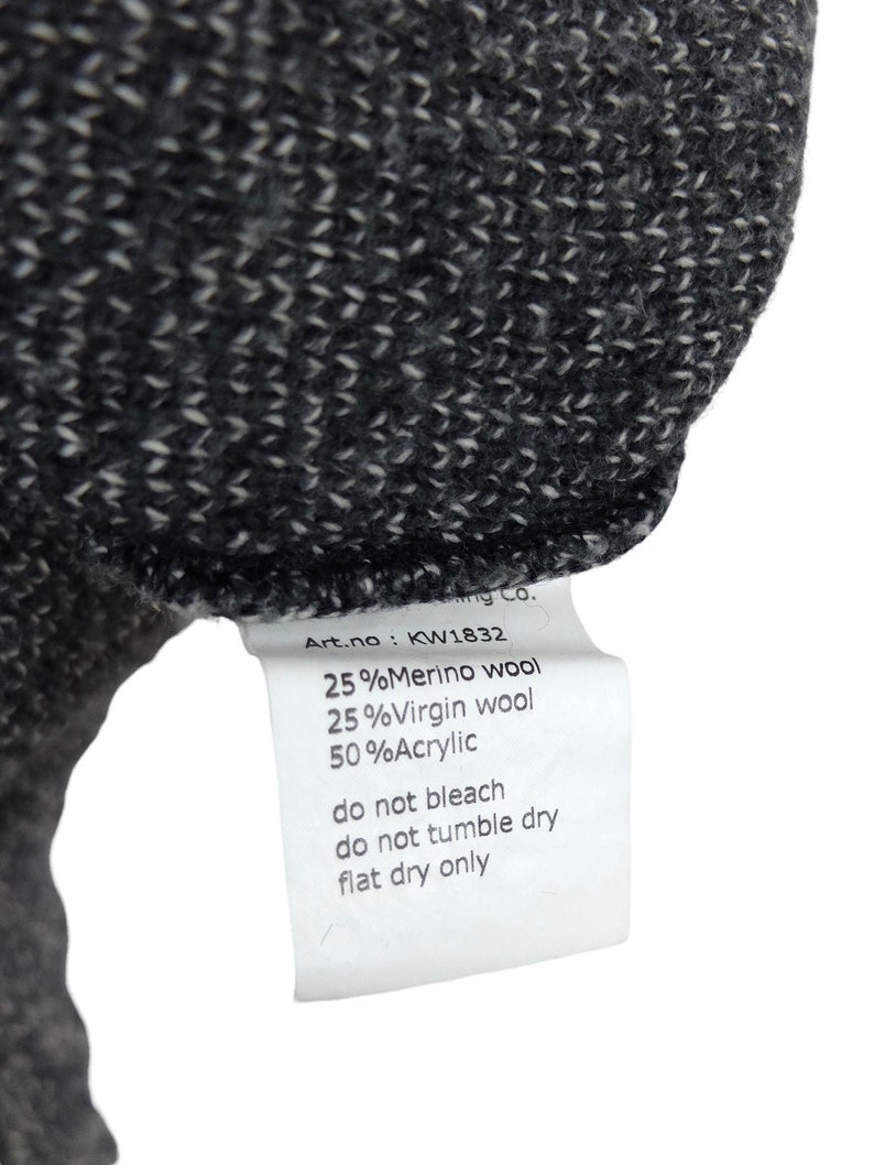 May include: A white tag with black text detailing the fabric composition and care instructions for a garment. The tag reads: "Art.no: KW1832 25%Merino wool 25%Virgin wool 50%Acrylic do not bleach do not tumble dry flat dry only"