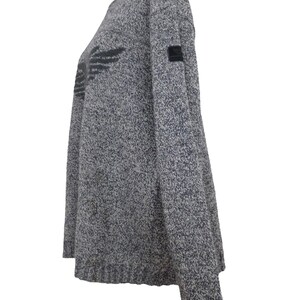 May include: A gray and white speckled sweater with a black wing design on the front. The sweater has a crew neck and long sleeves.