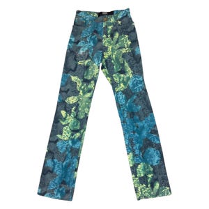 May include: High-waisted denim jeans with a vibrant pattern. The jeans feature a repeating design of blue and green floral and leaf shapes on a gray background. The jeans have a classic five-pocket design and a button and zipper closure.