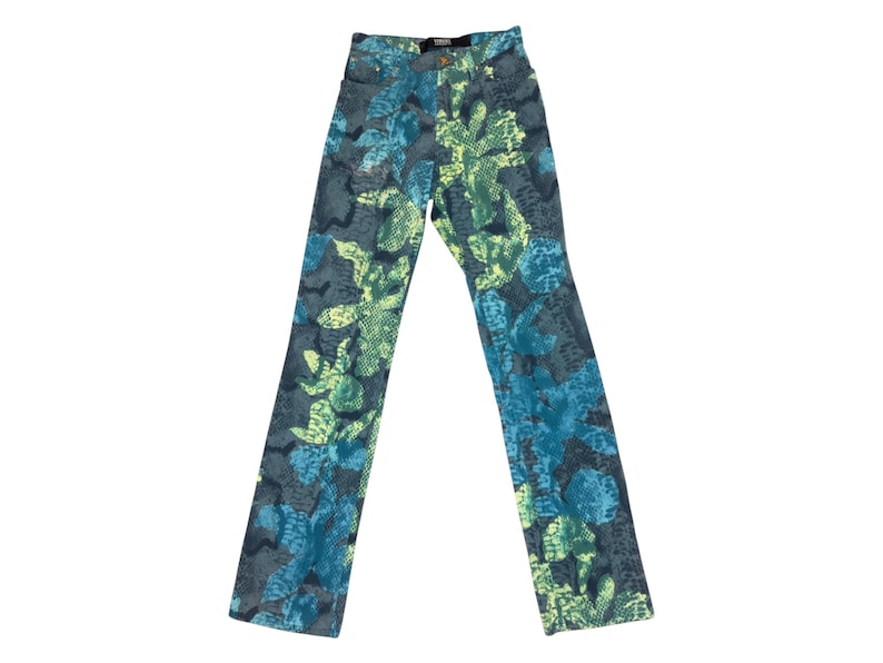 May include: High-waisted denim jeans with a vibrant pattern. The jeans feature a repeating design of blue and green floral and leaf shapes on a gray background. The jeans have a classic five-pocket design and a button and zipper closure.
