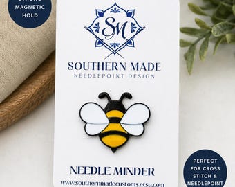 May include: A bee-shaped needle minder with black, yellow, and white details, displayed on a white card. The card features the text "SOUTHERN MADE NEEDLEPOINT DESIGN" and "NEEDLE MINDER". A blue circle reads "STRONG MAGNETIC HOLD".