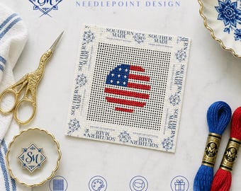 May include: A needlepoint design featuring a circular American flag. The canvas is surrounded by text that reads "SOUTHERN MADE NEEDLEPOINT DESIGN." Accessories include gold scissors, thread spools, and a small dish. The design is hand-painted and proudly made in the USA.
