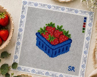 May include: A needlepoint canvas featuring a blue basket overflowing with red strawberries and green leaves. The canvas has a blue border with the text "SOUTHERN MADE". The initials "SR" are visible. Other items include embroidery floss, scissors, and a needlepoint tool.