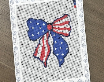 May include: Needlepoint canvas featuring a patriotic bow design. The bow is rendered in red and white stripes and blue with white stars, evoking the American flag. The canvas is bordered with the text "SOUTHERN MADE".
