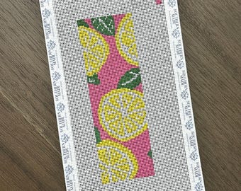 May include: Needlepoint canvas with a pink background and a pattern of yellow lemons and green leaves. The canvas is rectangular with a white border that has the text "SOUTHERN MADE" printed on it.