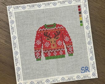 May include: A square needlepoint canvas featuring a red sweater design with a central reindeer graphic, white snowflake patterns, and green trim. The border is printed with the text Southern Made, and a color palette guide is visible on the right side.