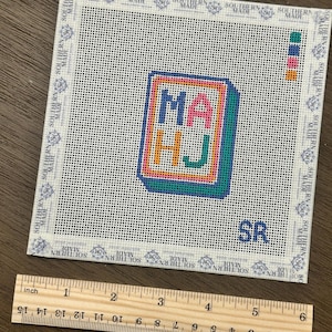 May include: A needlepoint canvas with the letters "MA HJ" in a colorful, framed design. The canvas is white with a grid pattern and the text "SOUTHERN MADE" around the border. A wooden ruler shows the canvas is approximately 5 inches wide.