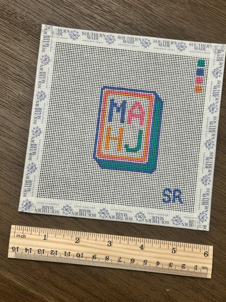 May include: A needlepoint canvas with the letters "MA HJ" in a colorful, framed design. The canvas is white with a grid pattern and the text "SOUTHERN MADE" around the border. A wooden ruler shows the canvas is approximately 5 inches wide.