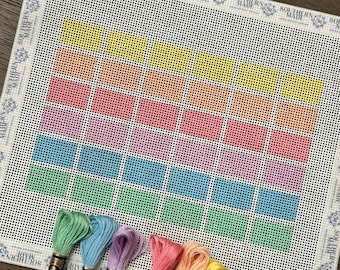 May include: A white needlepoint canvas featuring a grid of thirty-five rectangular color blocks in yellow, orange, pink, blue, and green. Six skeins of embroidery floss in matching colors are arranged at the bottom, each with a paper label.